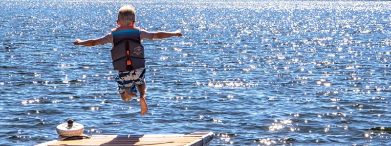 A boy jumps off a dock into a blue water of a lake