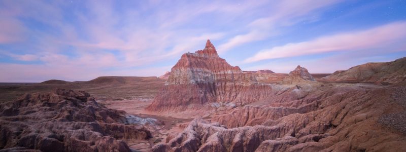 A red butte under a cloud-streaked blue sky in Wyoming's Red Desert